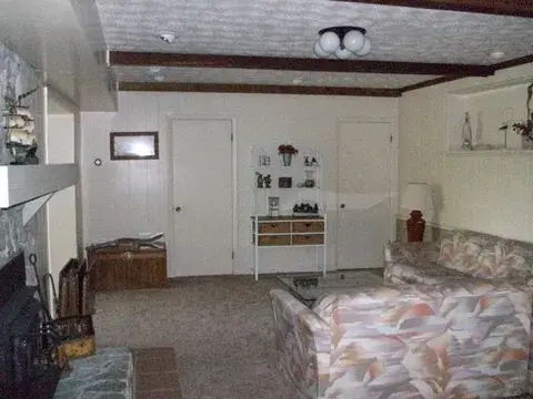 Family room before: dated patterned sofa, carpet, and wood-beamed ceiling